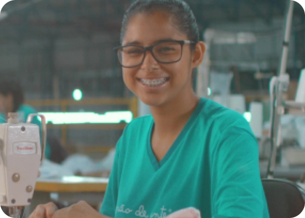 Imagem de uma mulher sorrindo e costurando na fábrica da Grão de Gente